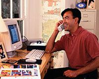 Obrázek muže pracující na počítači, mluví na telefonu